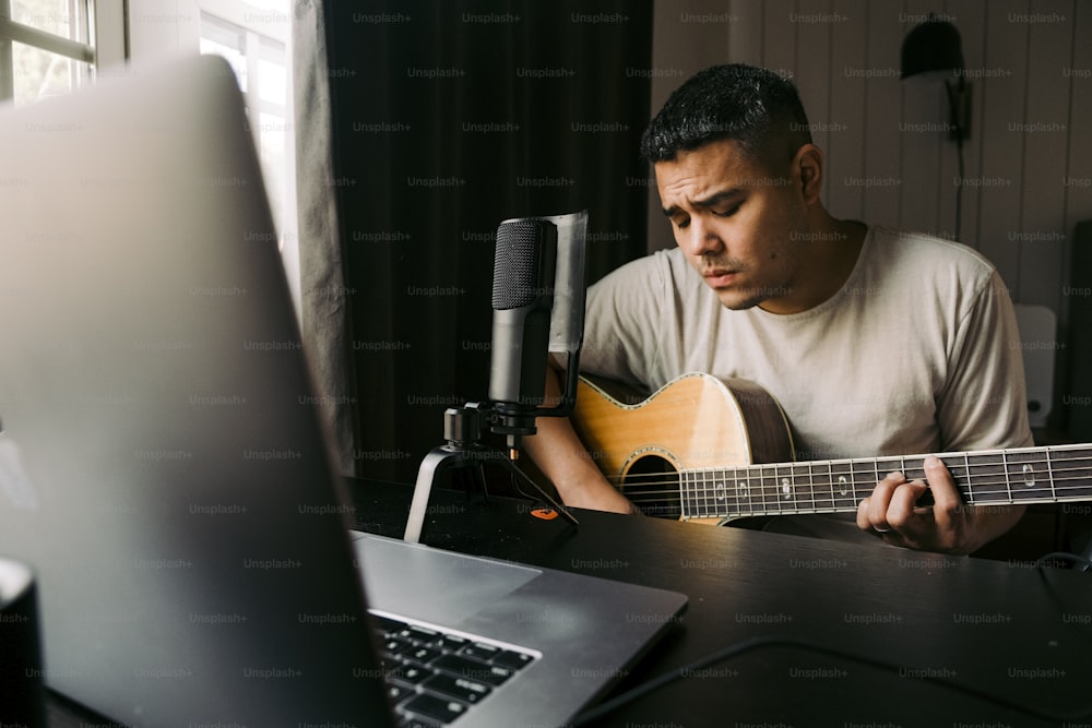 a man sitting in front of a laptop playing a guitar