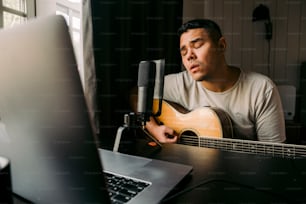 a man sitting in front of a laptop computer while holding a guitar