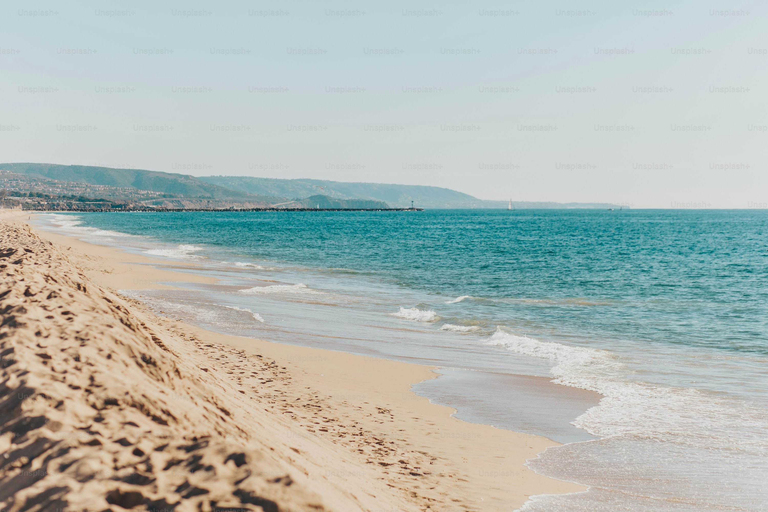 a sandy beach next to the ocean under a blue sky