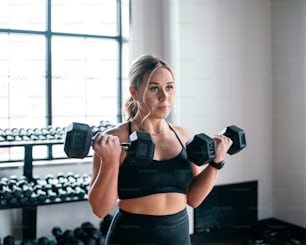 a woman holding two dumbs in a gym