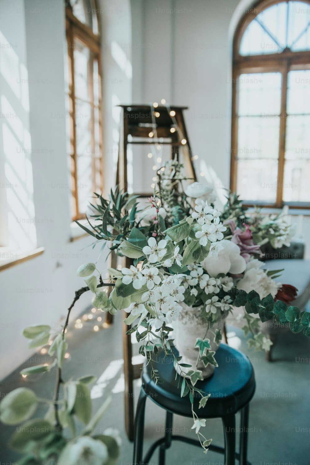 eine Vase gefüllt mit weißen Blumen, die auf einem blauen Hocker sitzt