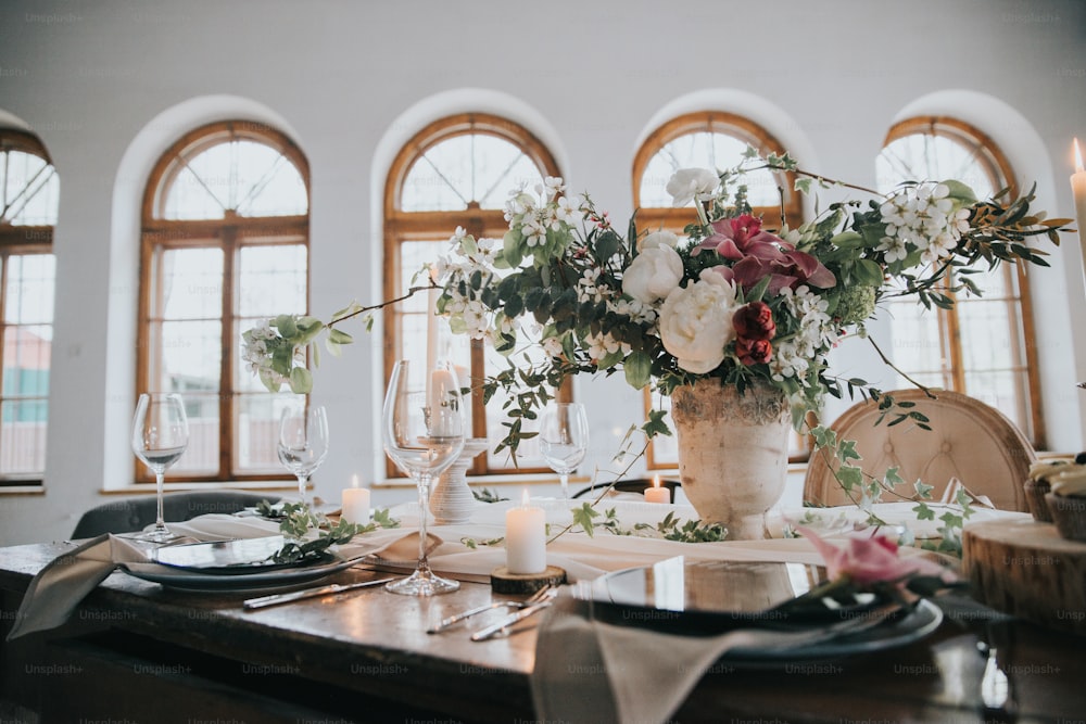 eine Vase mit Blumen auf einem Tisch mit Gedecken