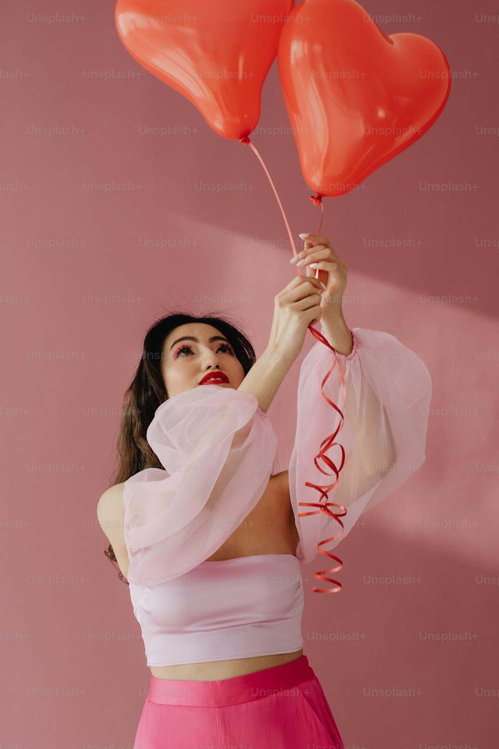 a woman holding two red heart shaped balloons