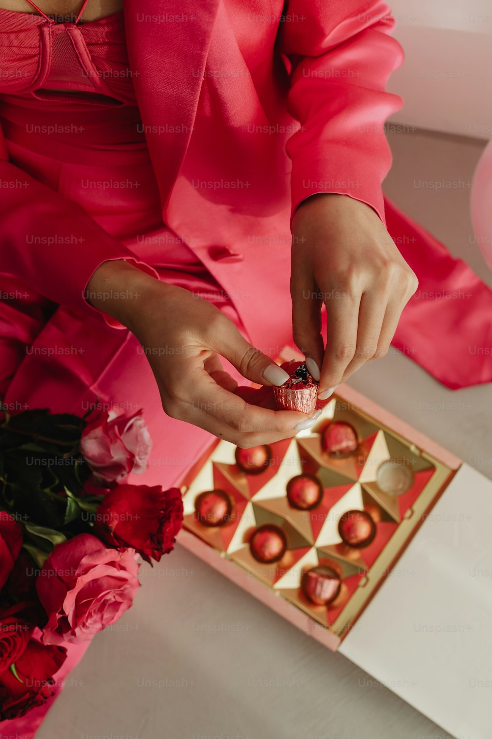 Une femme en costume rose tient une boîte de chocolats