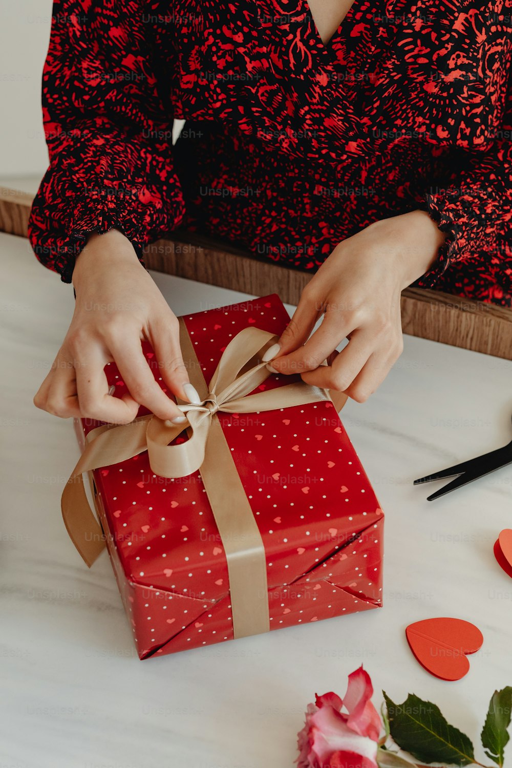 a woman wrapping a red gift box with a brown ribbon