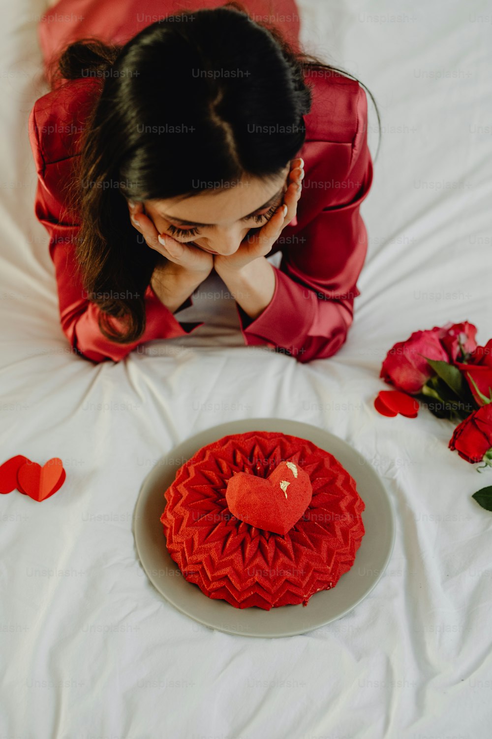 a woman sitting on a bed next to a heart shaped cake