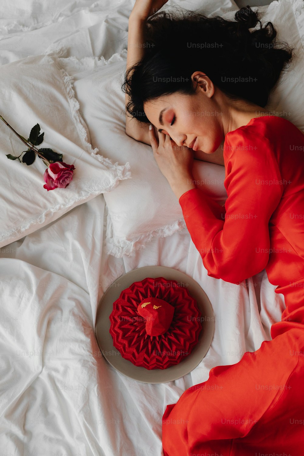 Una mujer acostada en una cama junto a un pastel rojo