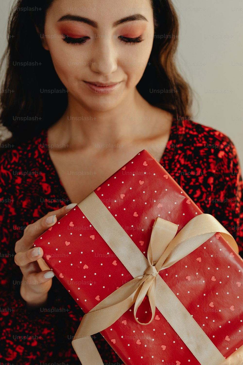 a woman holding a red gift box with a brown ribbon