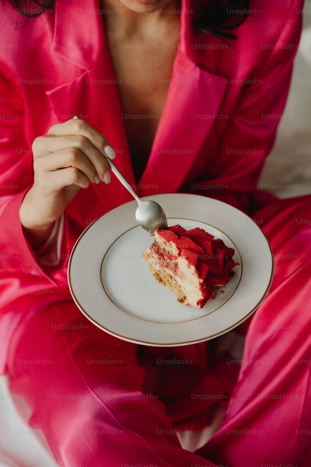uma mulher em um terno rosa segurando um prato com um pedaço de bolo sobre ele