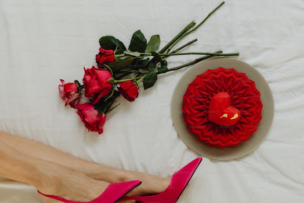 a woman's feet on a bed next to a red rose and a red