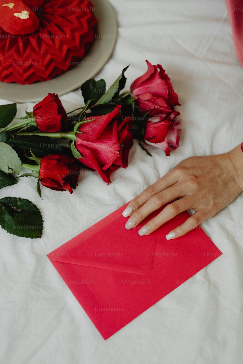 Eine Frauenhand auf einem roten Umschlag neben Rosen