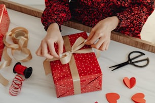 a woman is wrapping a red gift with a brown ribbon