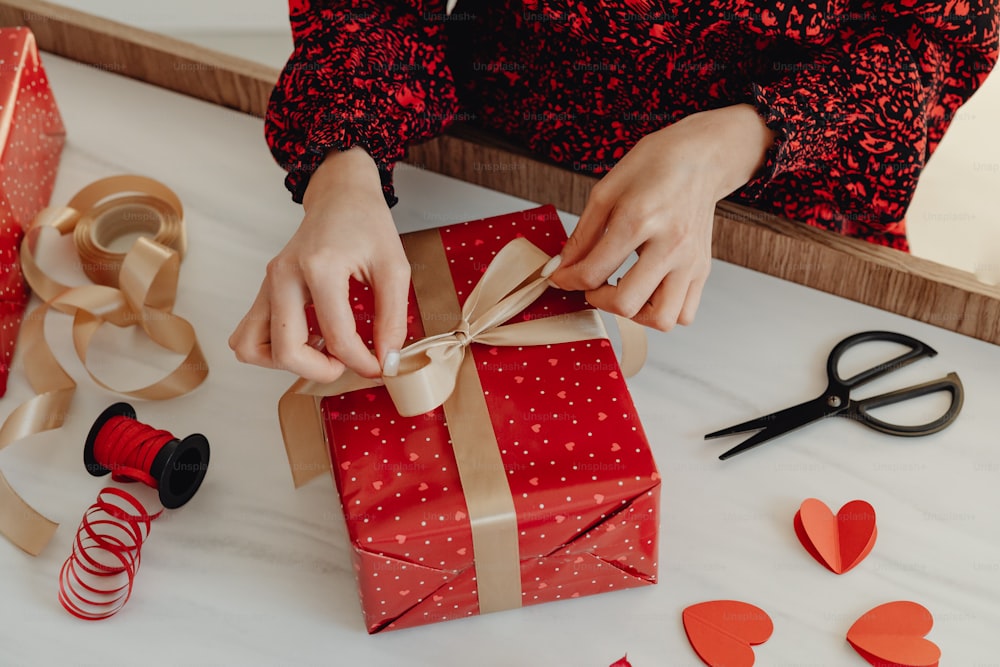 a woman is wrapping a red gift with a brown ribbon