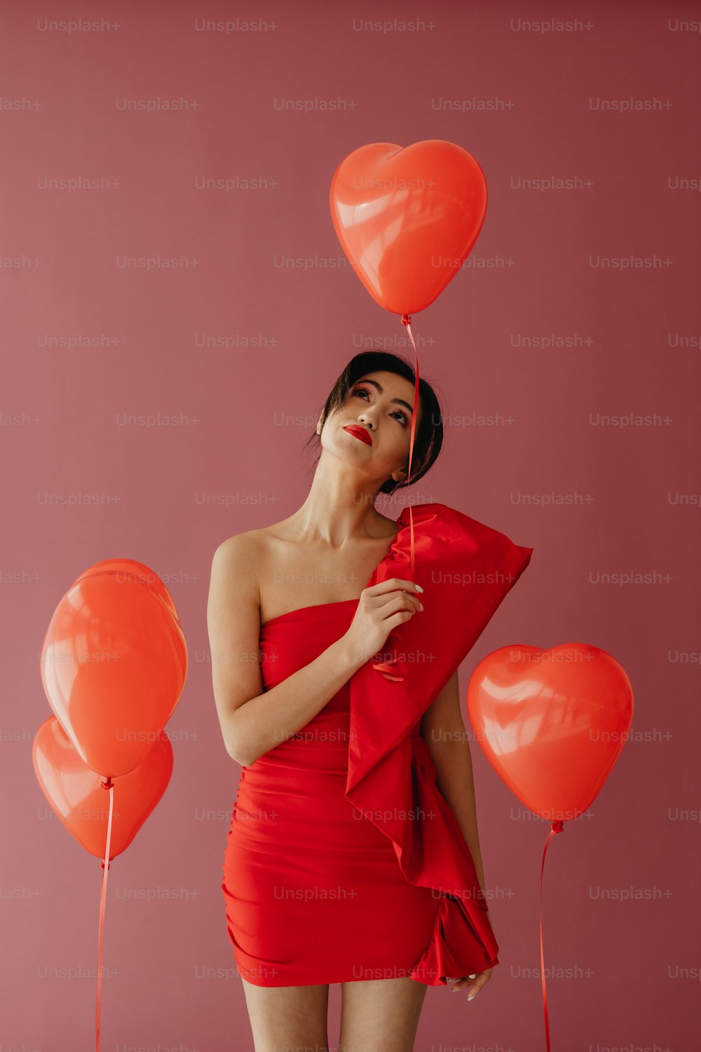 a woman in a red dress holding a bunch of balloons