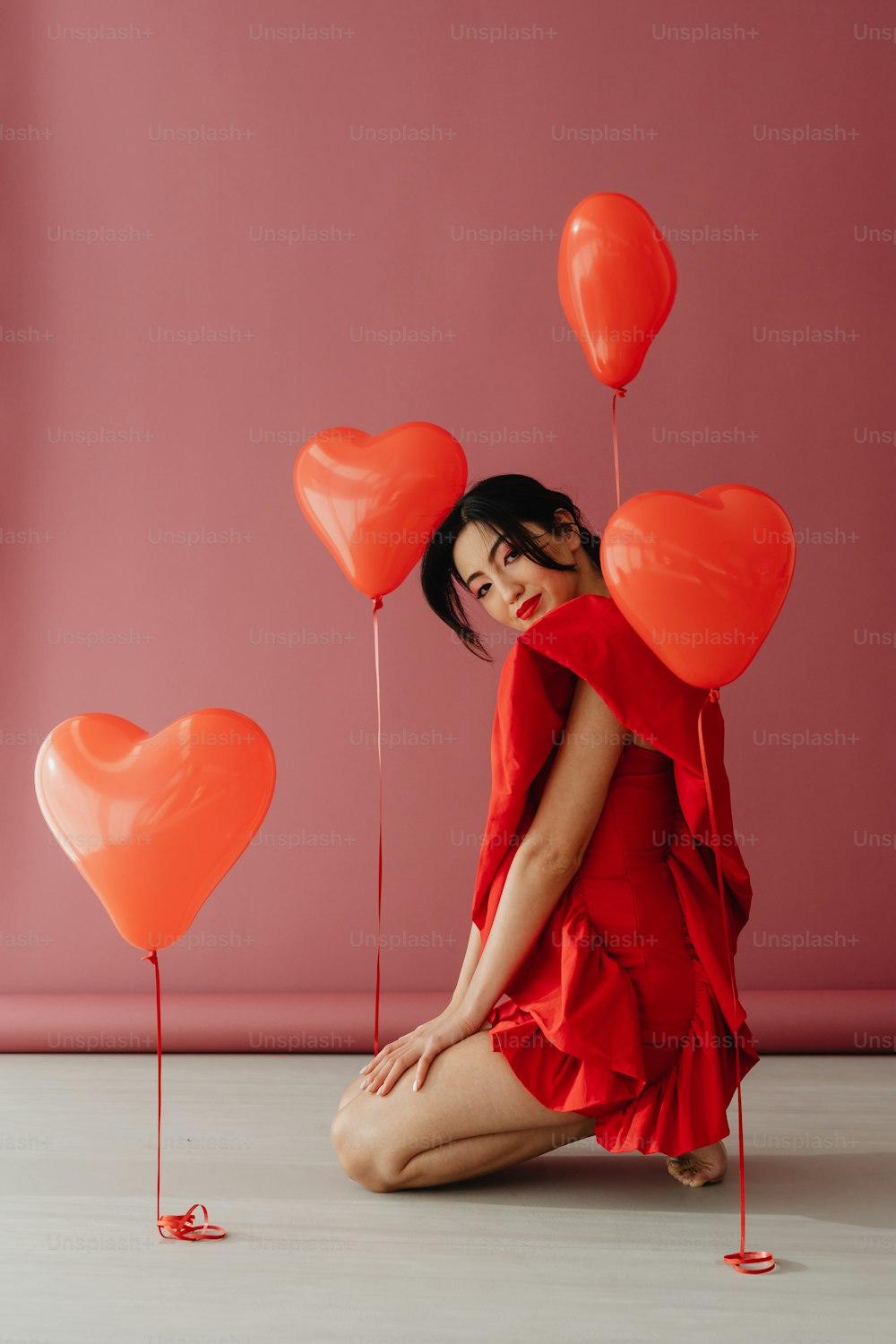 Una mujer con un vestido rojo sentada en el suelo con globos rojos