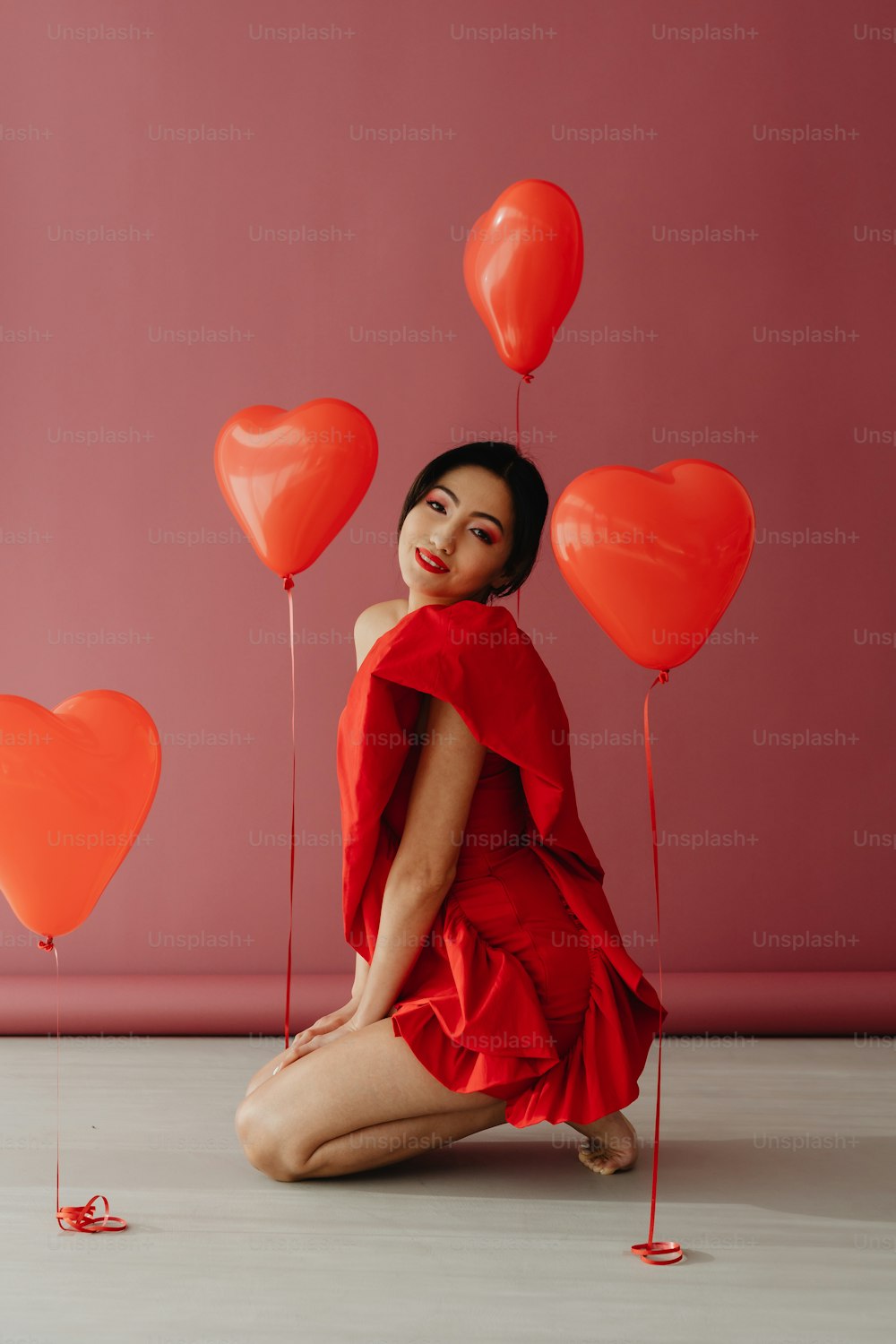 a woman in a red dress sitting on the floor with red balloons
