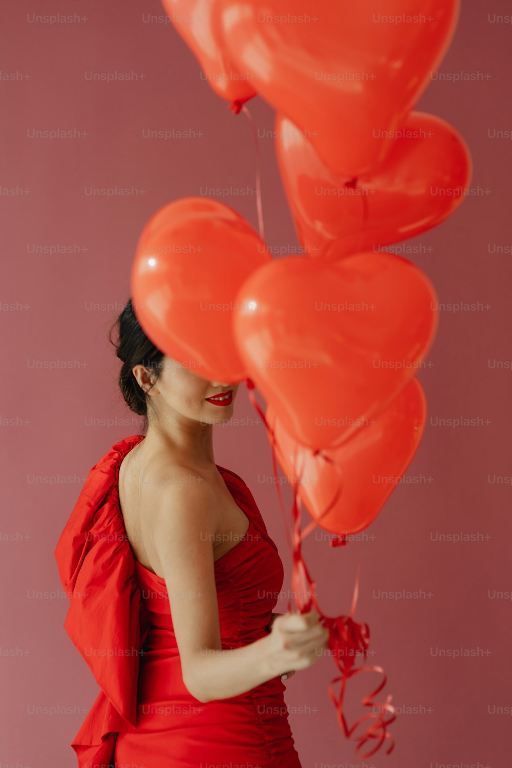 Eine Frau in einem roten Kleid, die einen Haufen roter Luftballons hält