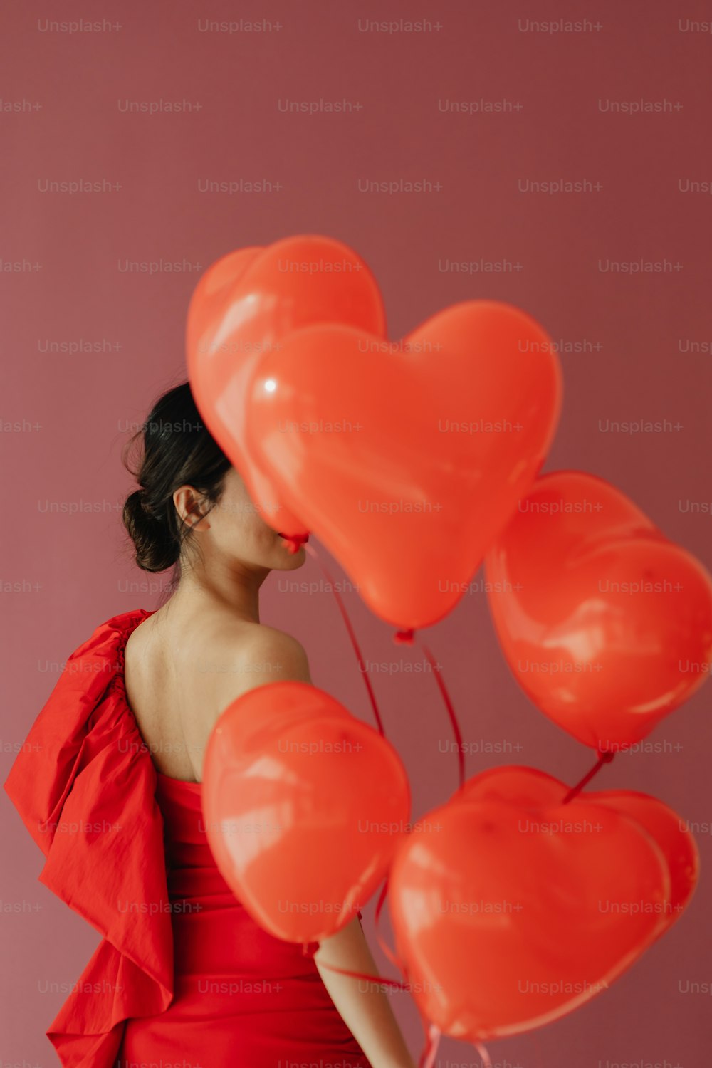 a woman in a red dress holding a bunch of heart shaped balloons