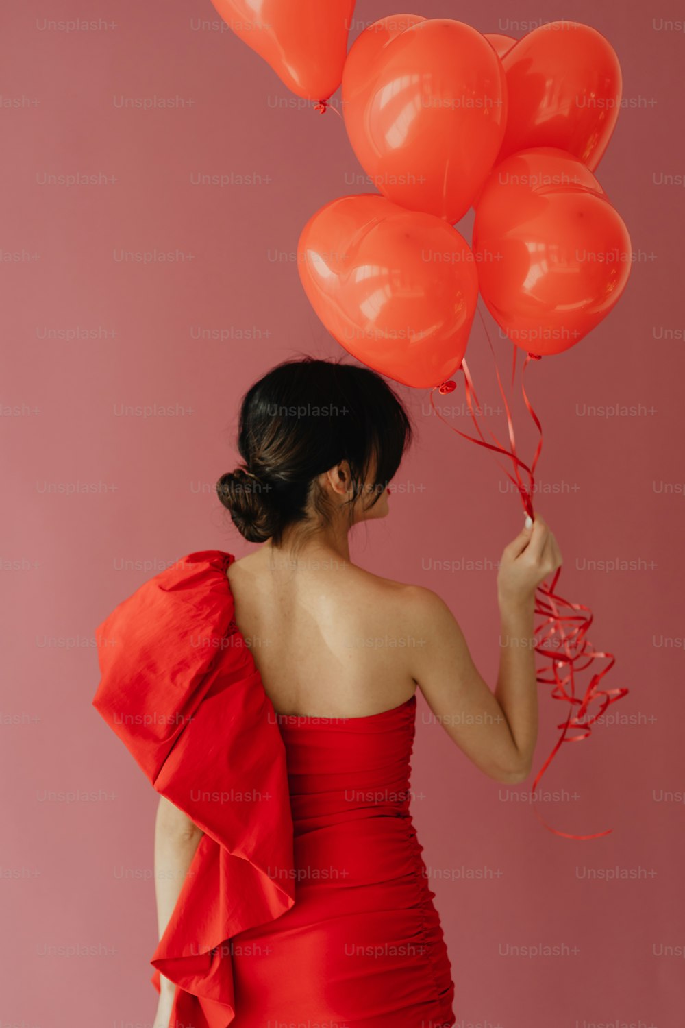 a woman in a red dress holding a bunch of red balloons