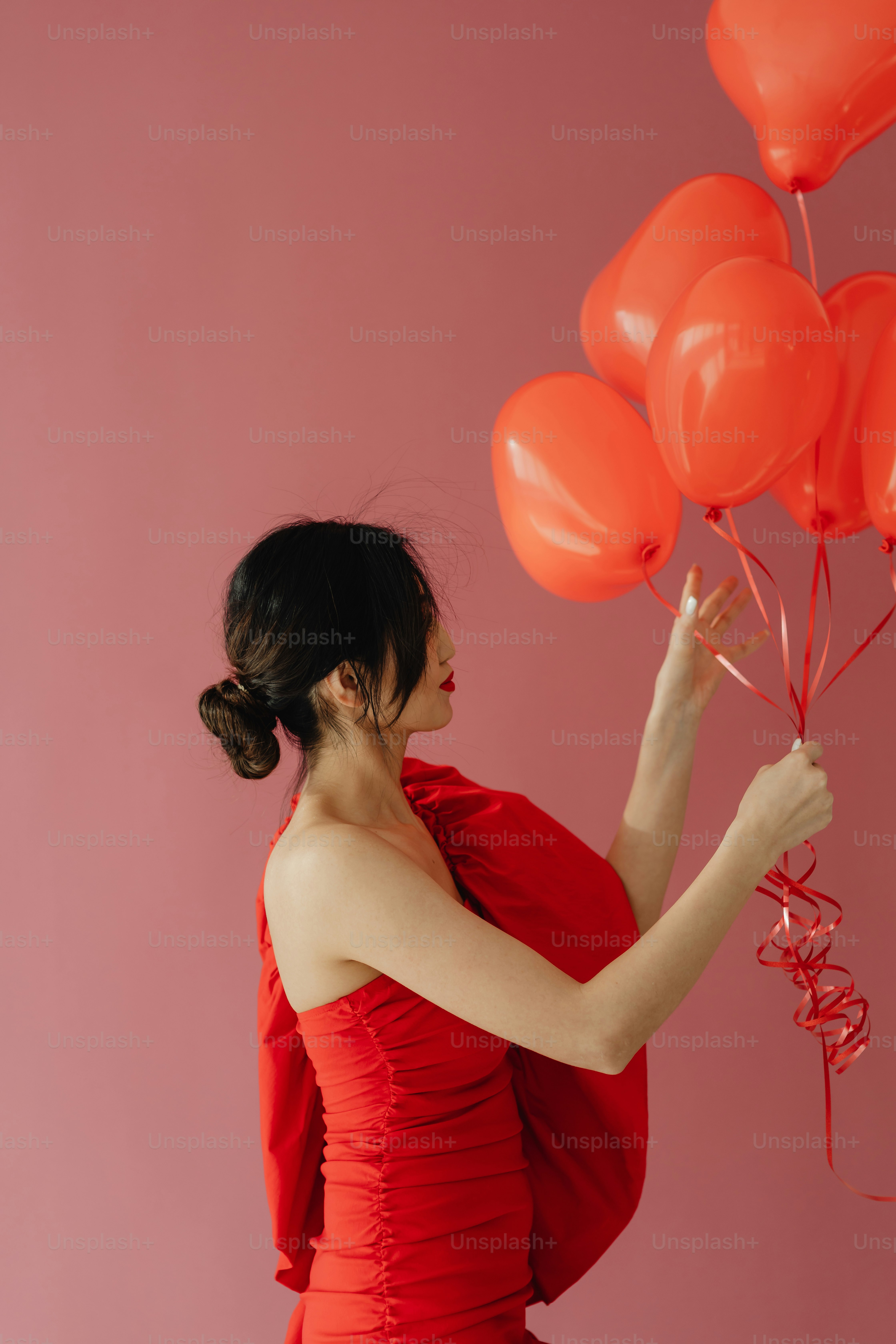 a woman in a red dress holding a bunch of red balloons