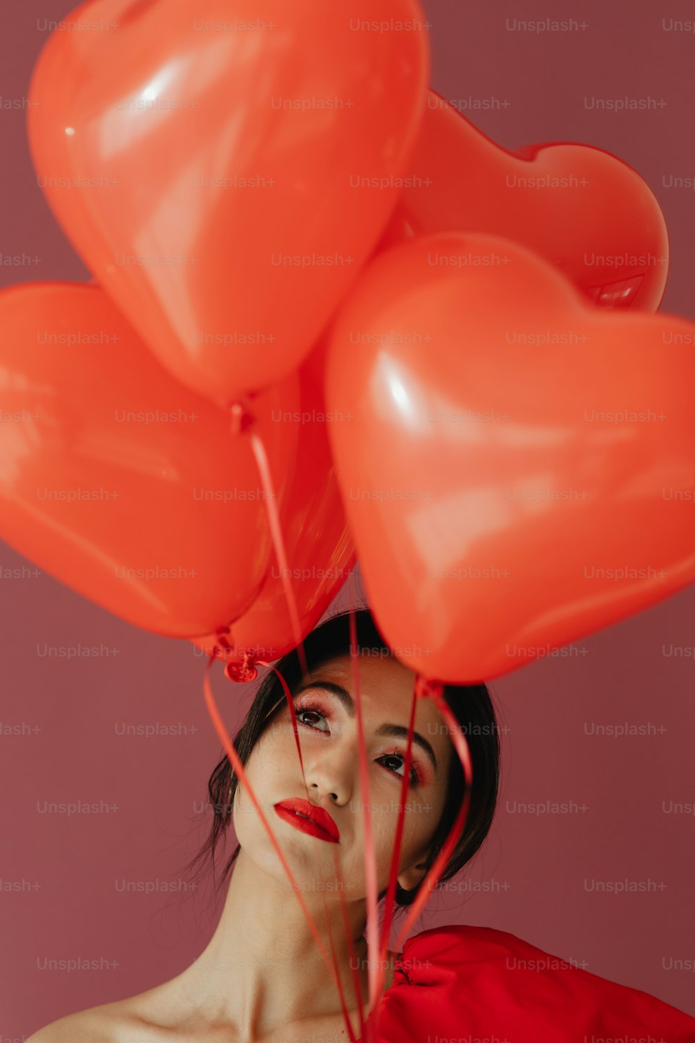 a woman holding a bunch of red heart shaped balloons