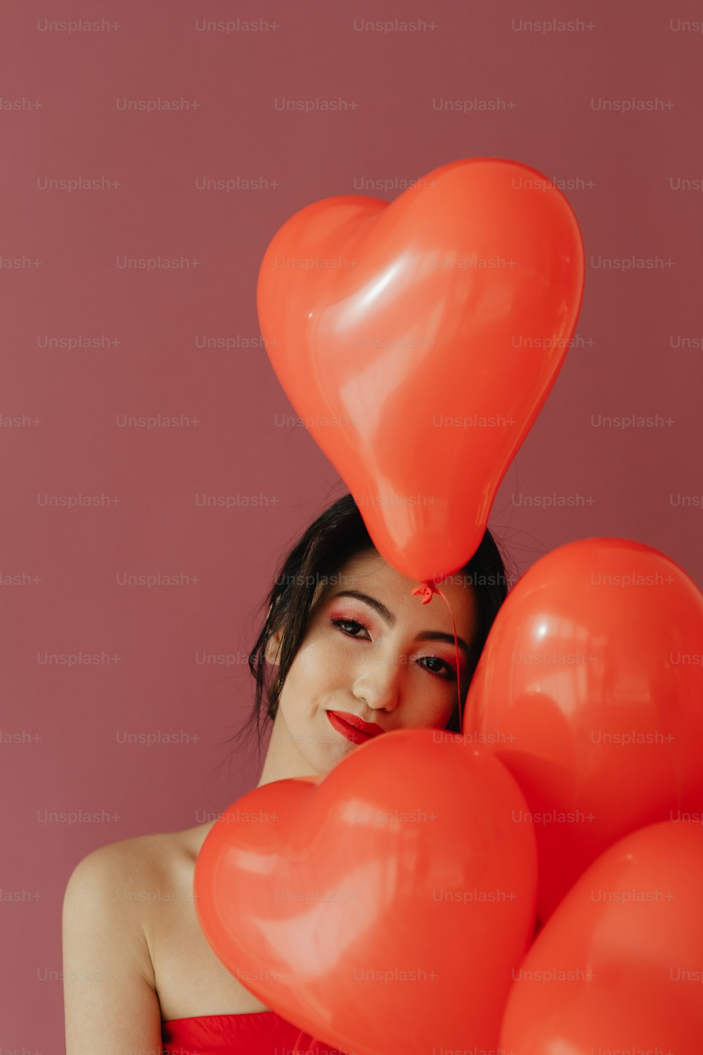 a woman in a red dress holding a bunch of red heart balloons