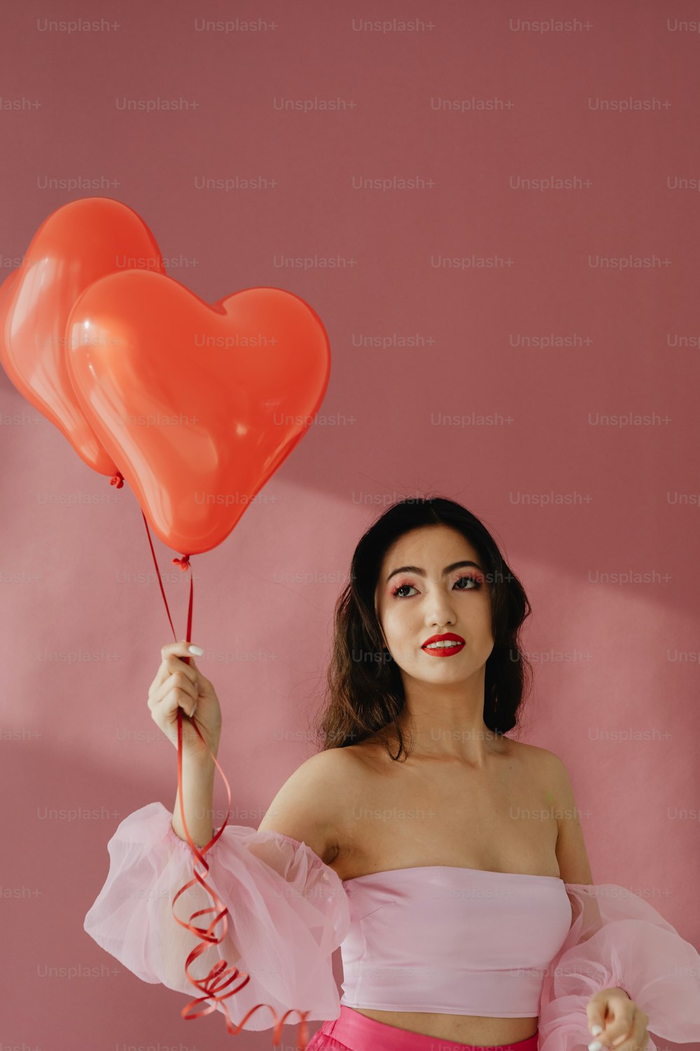 a woman in a pink dress holding two heart shaped balloons