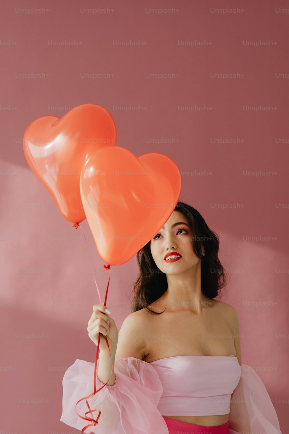 a woman in a pink dress holding two heart shaped balloons