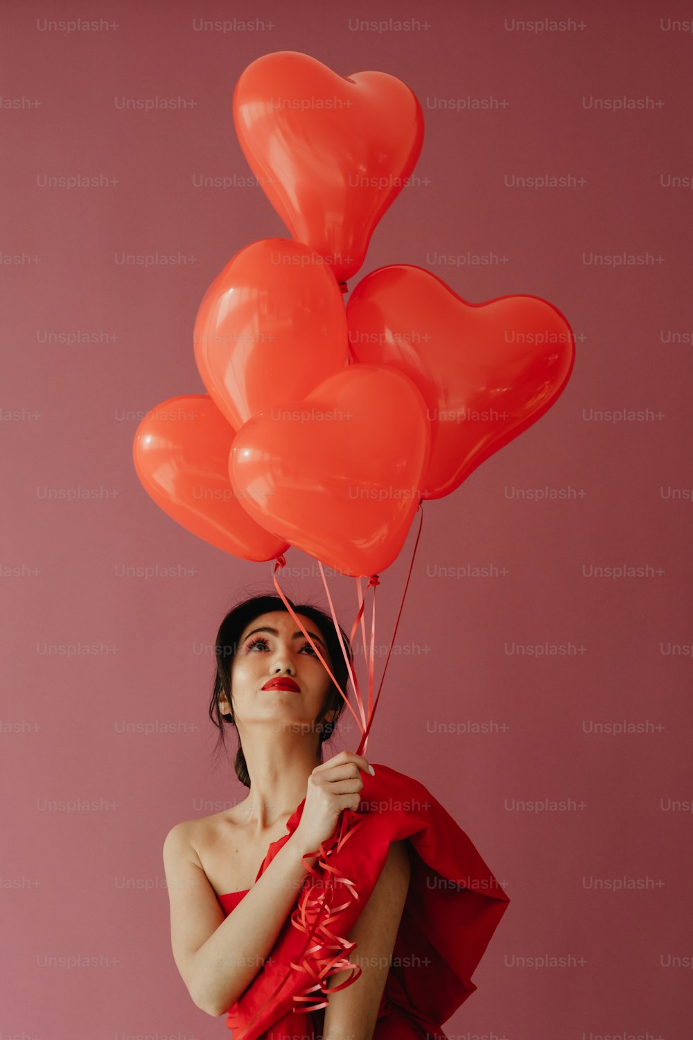 a woman holding a bunch of red heart balloons