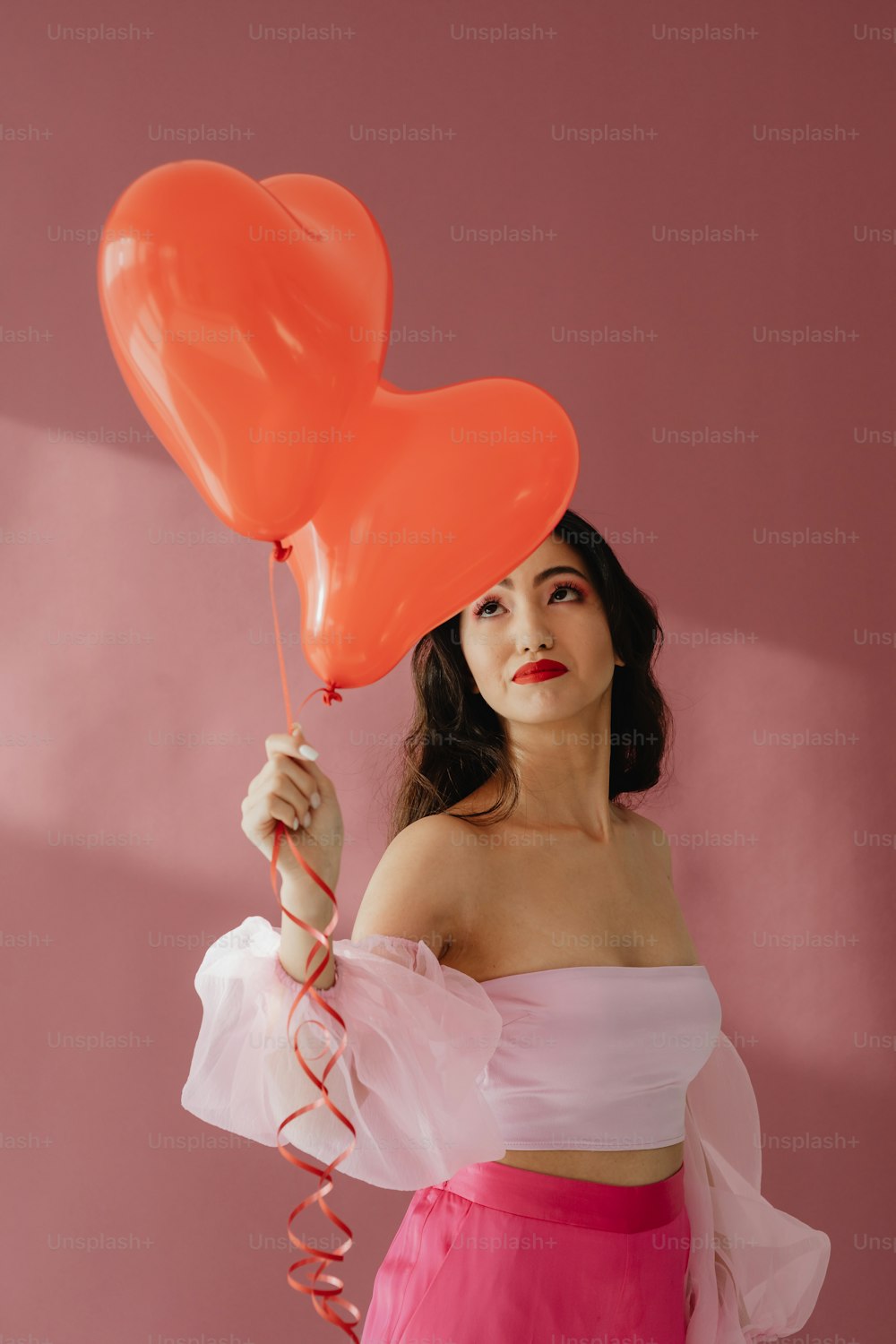 a woman in a pink dress holding a heart shaped balloon