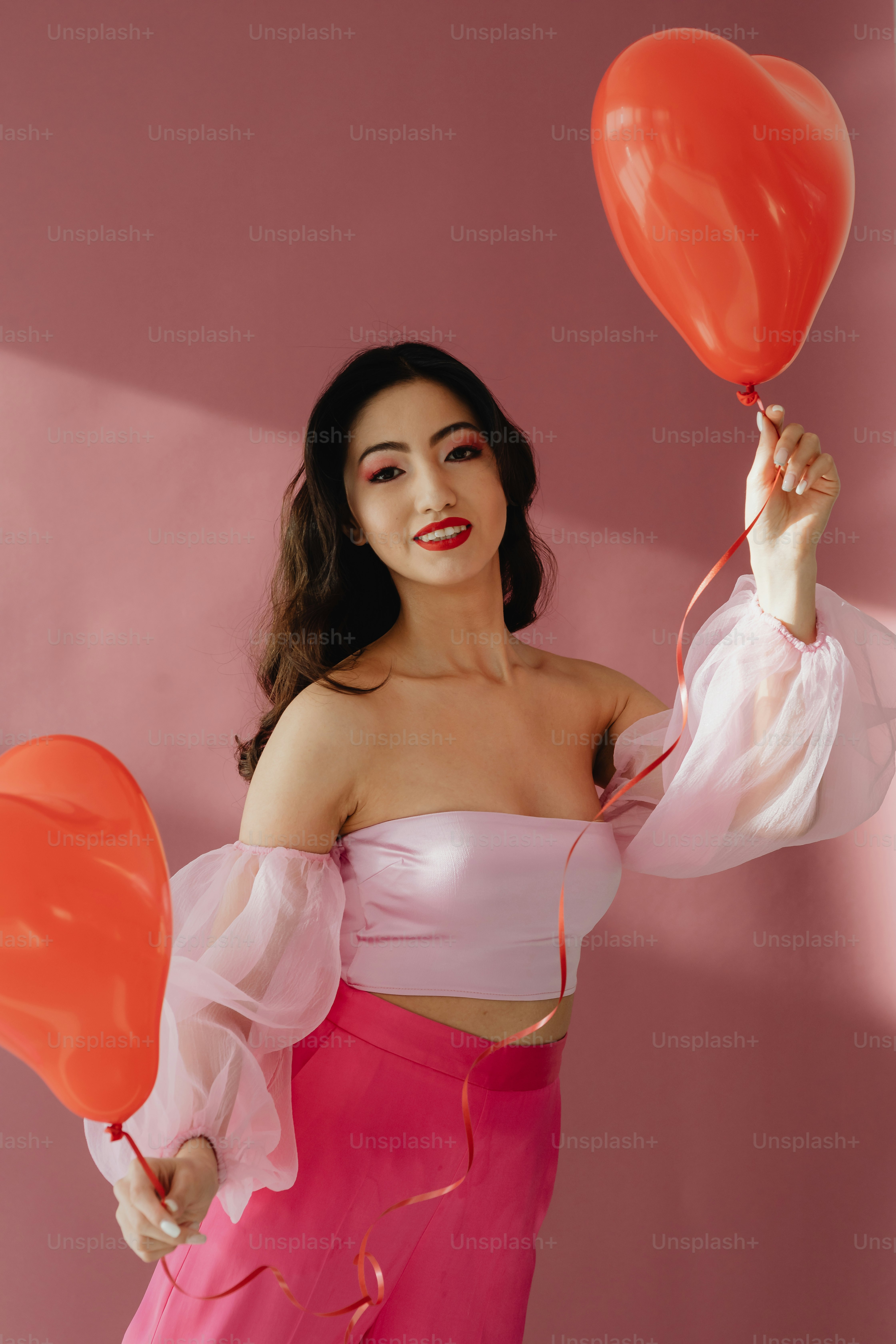Una mujer con un vestido rosa sosteniendo dos globos rojos