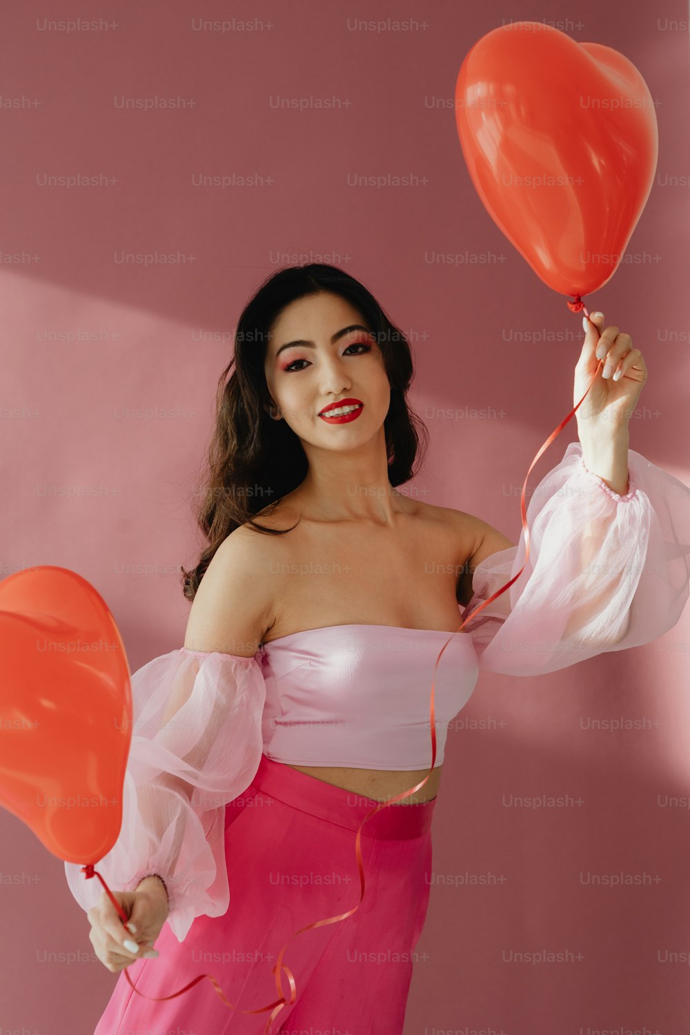 a woman in a pink dress holding two red balloons