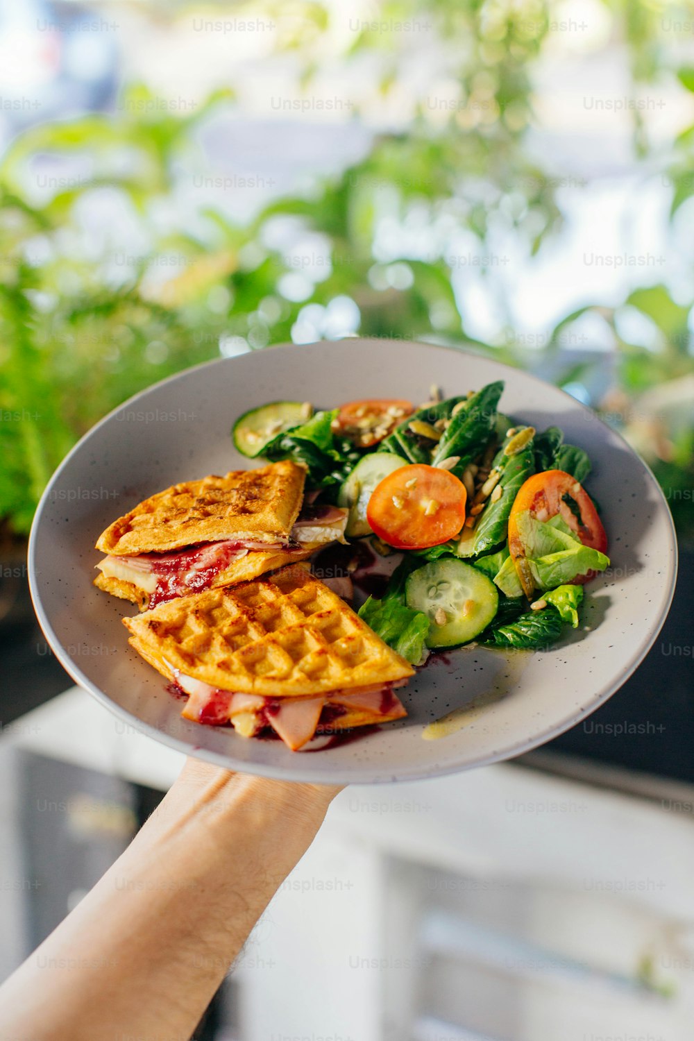 a person holding a plate of food with waffles and vegetables