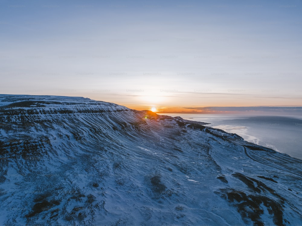 the sun is setting over a snowy mountain