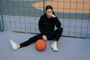 a woman sitting on the ground next to a basketball