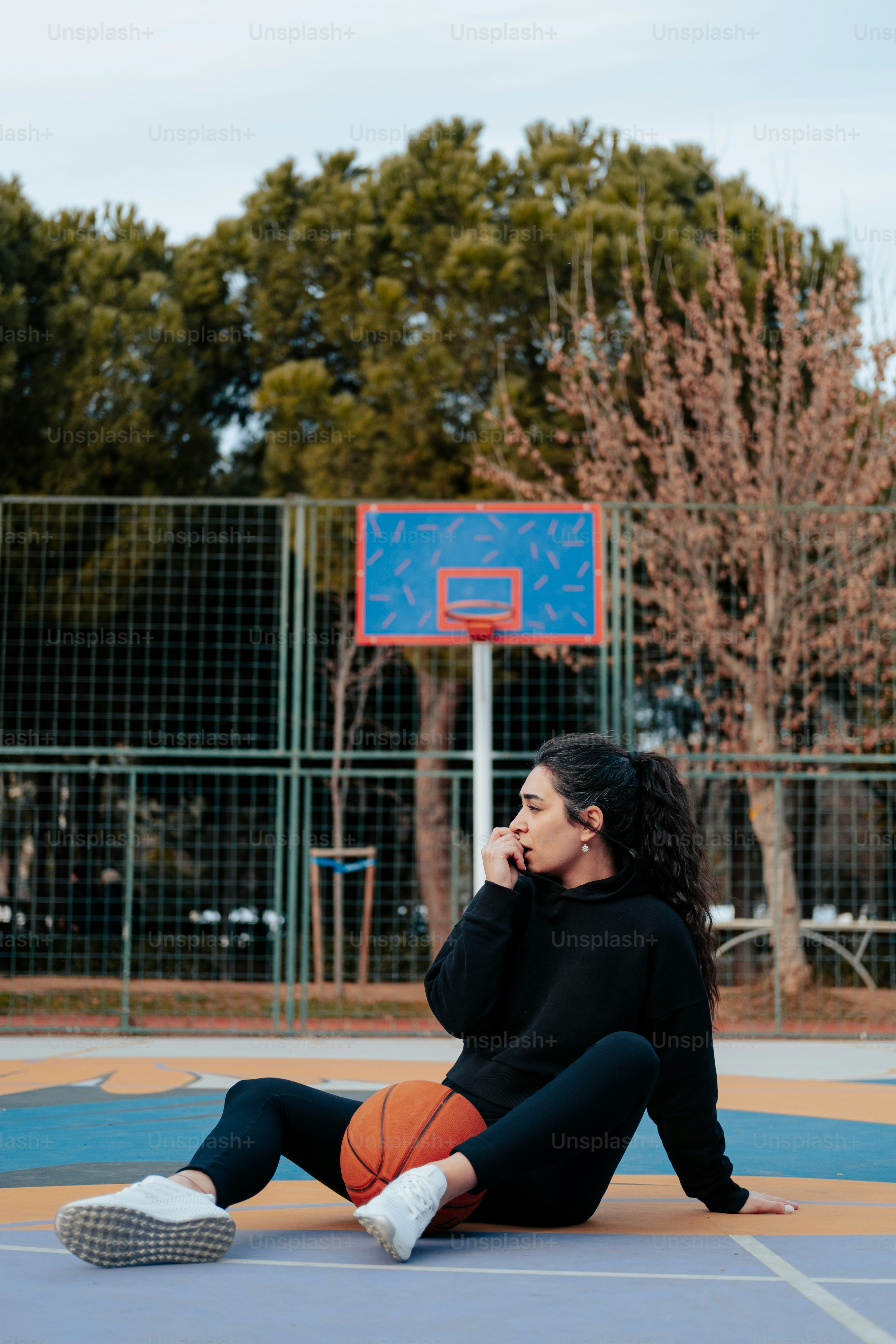 a woman sitting on a basketball court holding a basketball