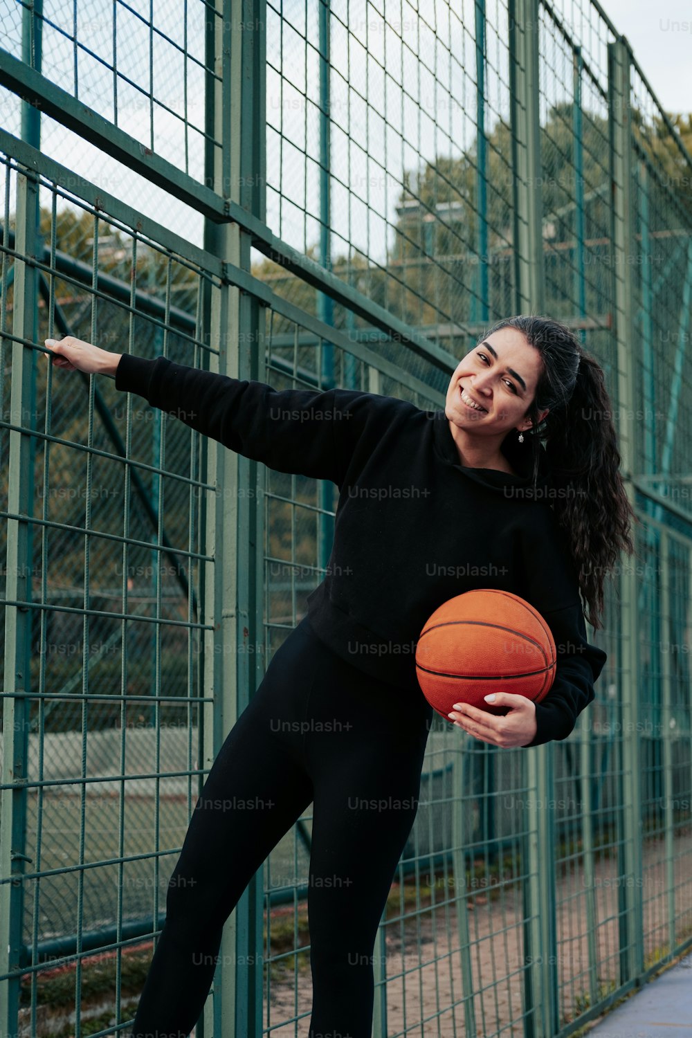 Una donna che tiene un pallone da basket in piedi vicino a una recinzione