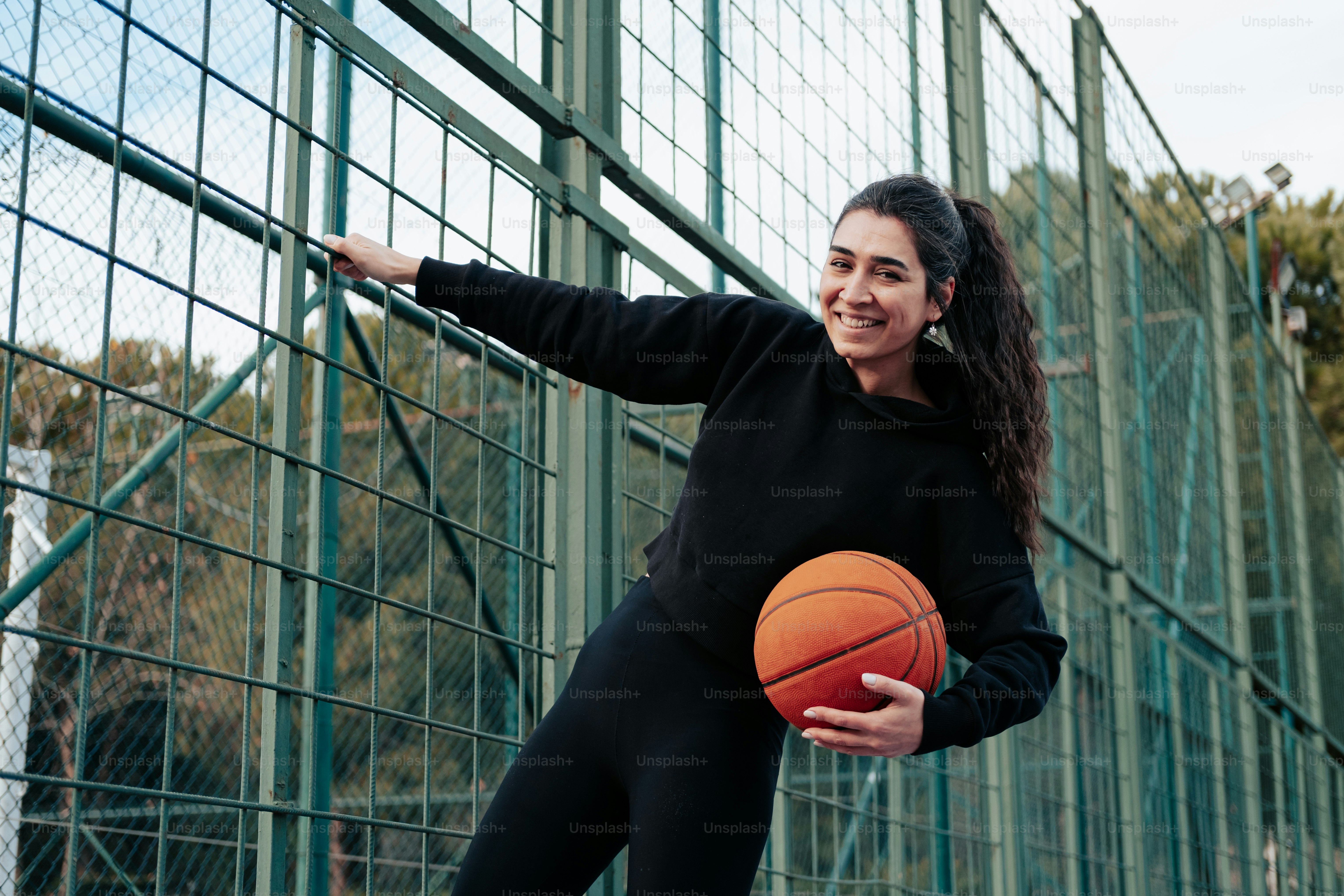 a woman holding a basketball standing next to a fence