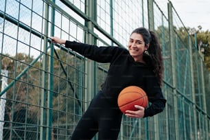a woman holding a basketball standing next to a fence