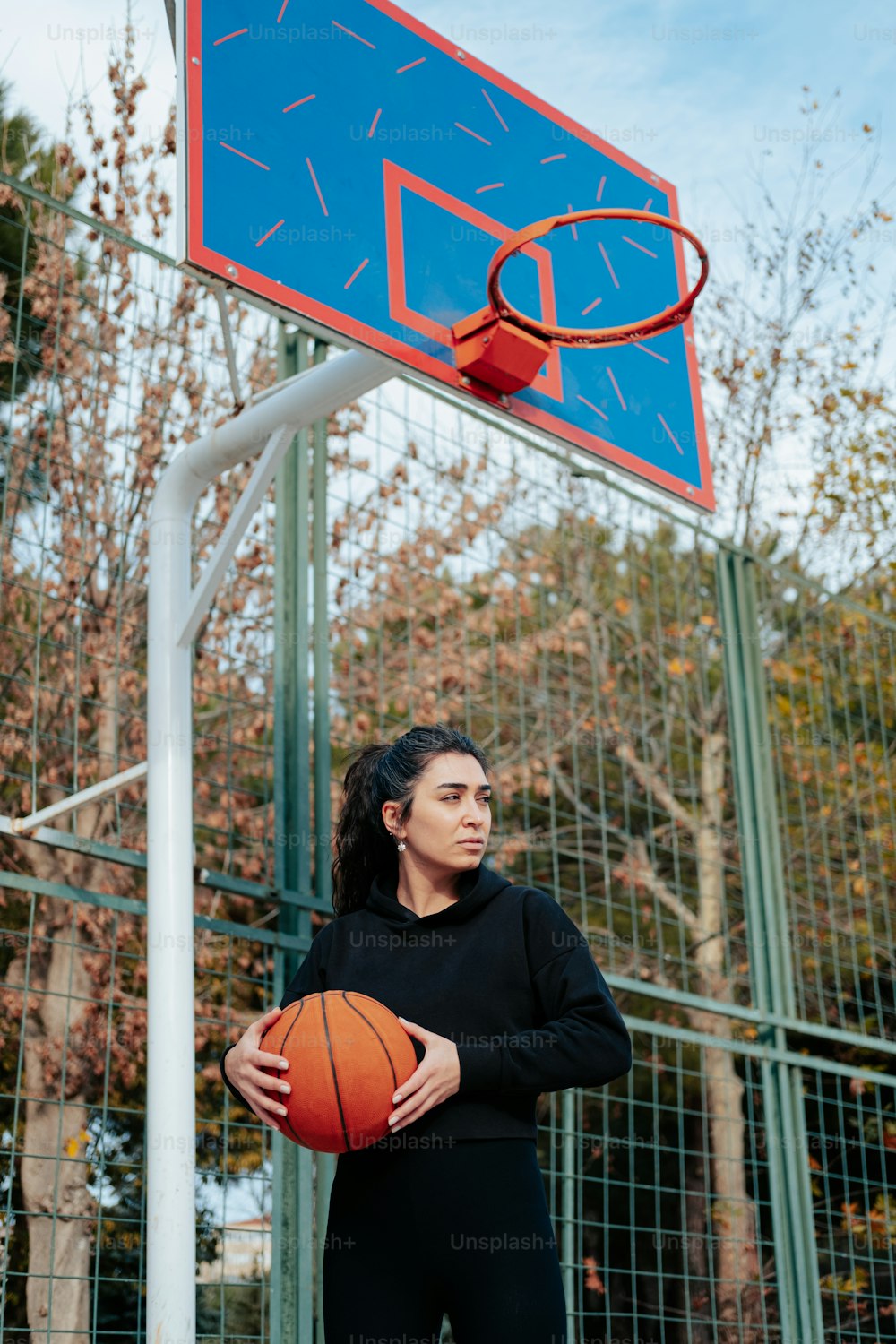 Una mujer sosteniendo una pelota de baloncesto frente a un aro de baloncesto