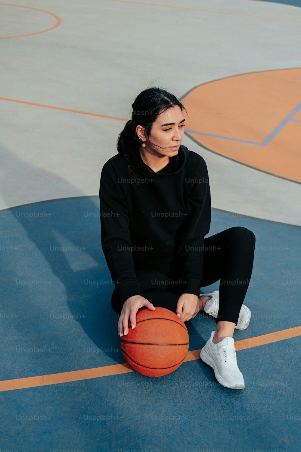 Une femme assise sur un terrain de basket-ball tenant un ballon de basket-ball