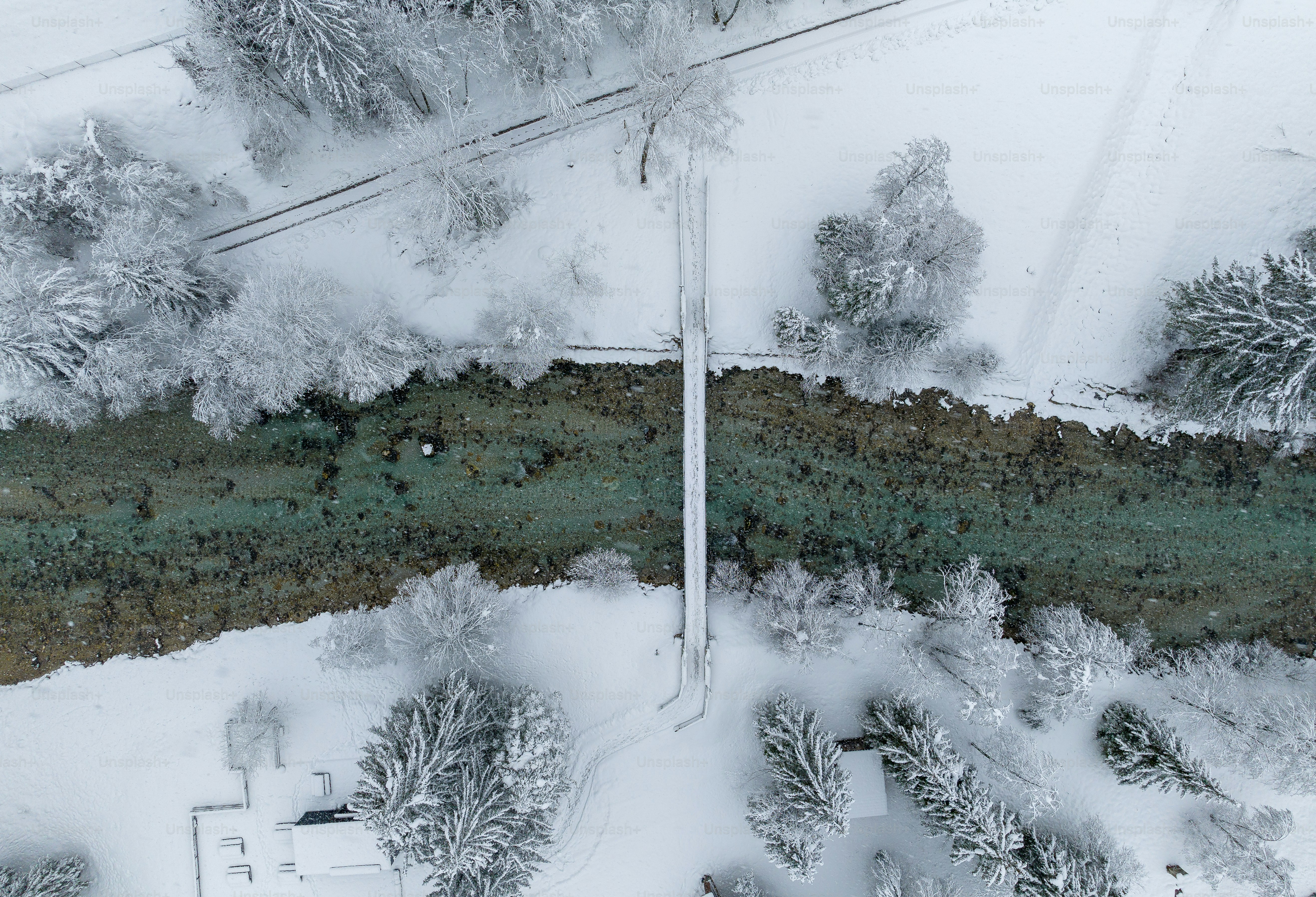 Snowing by the river on a cloudy winter day. A bridge over the river is used by hikers.