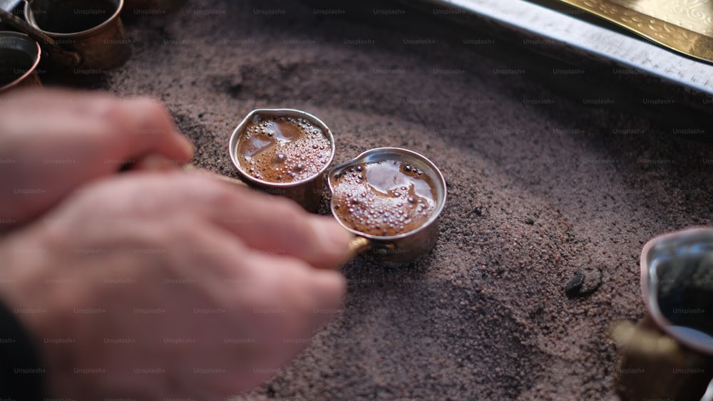 uma pessoa segurando uma colher sobre duas xícaras de café