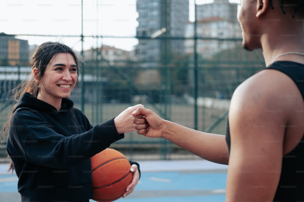 um homem e uma mulher apertando as mãos sobre uma bola de basquete