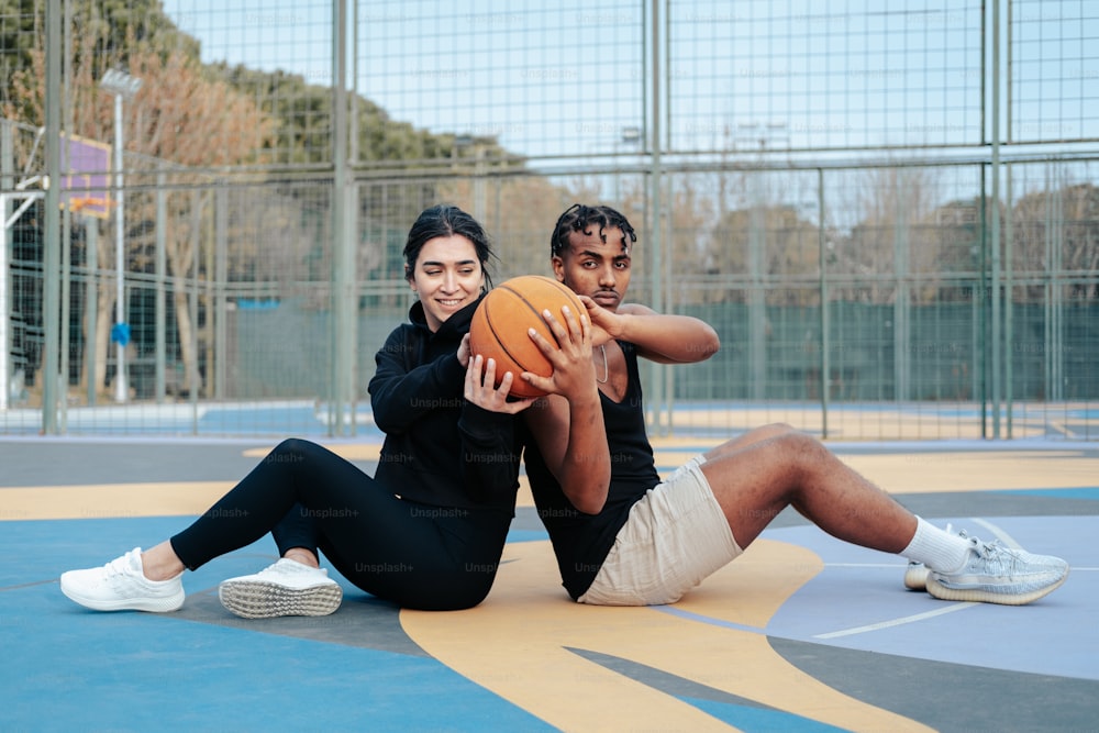 a man and woman sitting on the ground holding a basketball