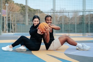a man and a woman sitting on the ground with a basketball