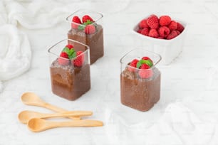 Trois verres de pudding au chocolat avec des framboises sur le dessus