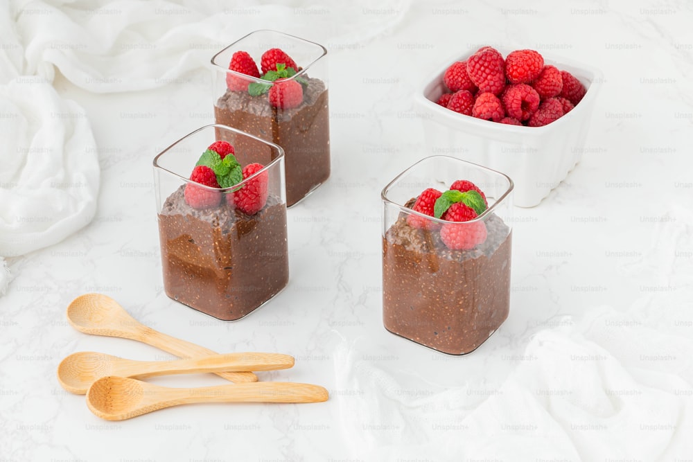 three glasses of chocolate pudding with raspberries on top