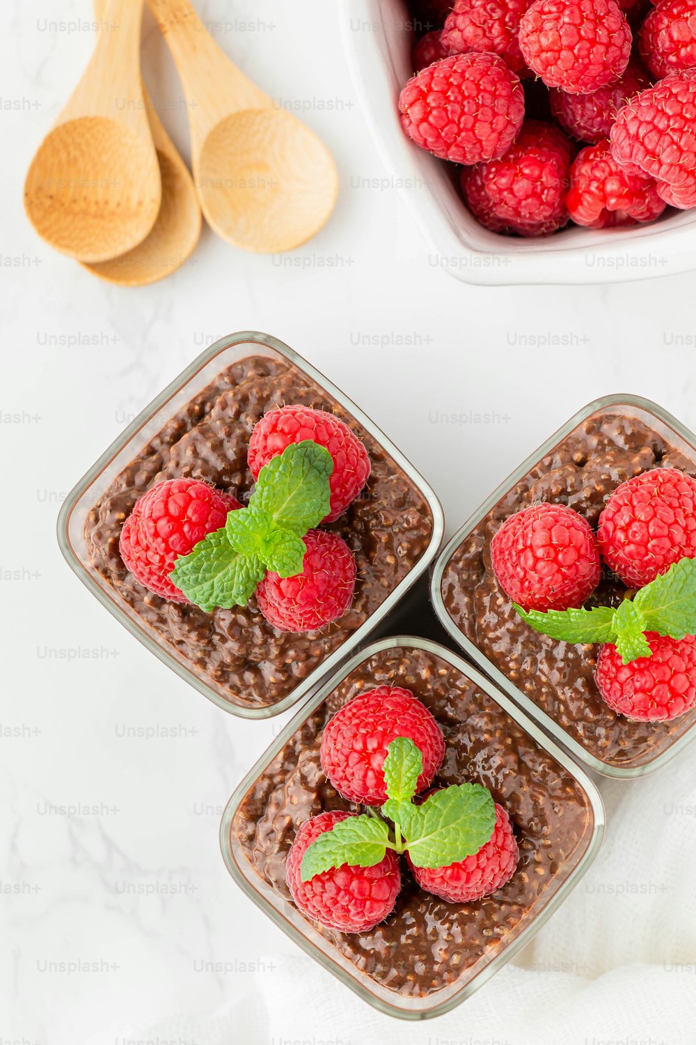 four small glass containers filled with chocolate pudding and raspberries