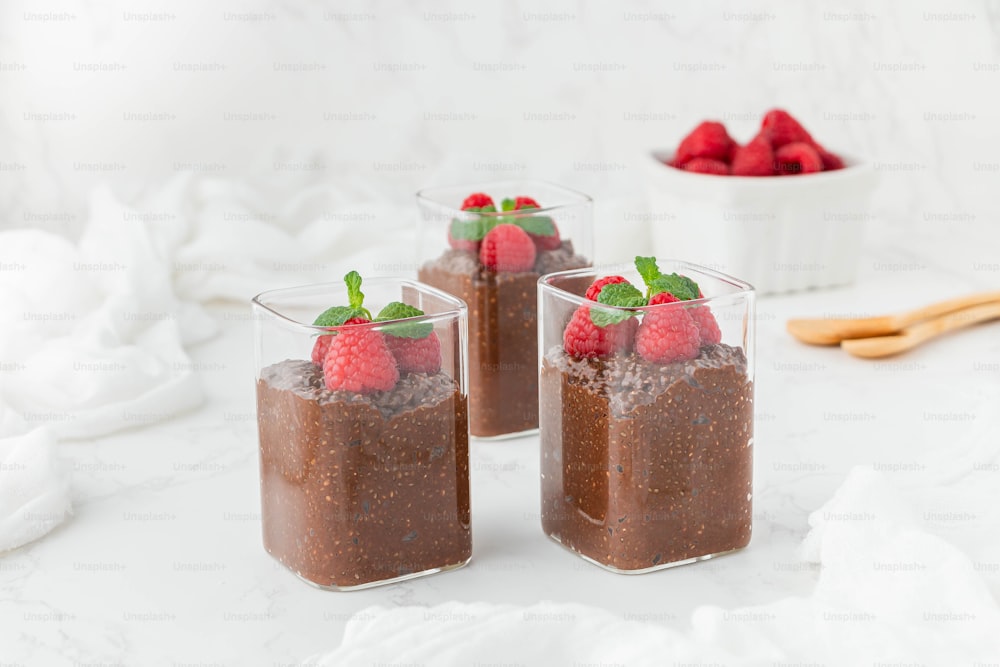 three glasses of chocolate pudding with raspberries on top